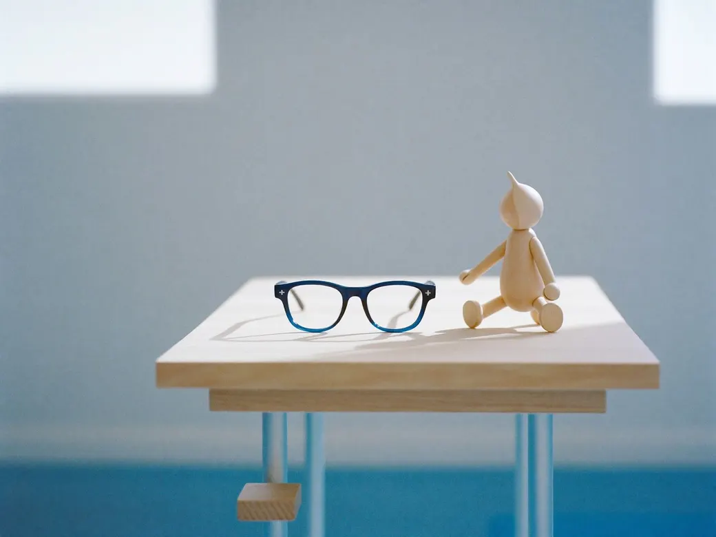 Lentes infantiles de armazón azul junto a un muñeco de madera