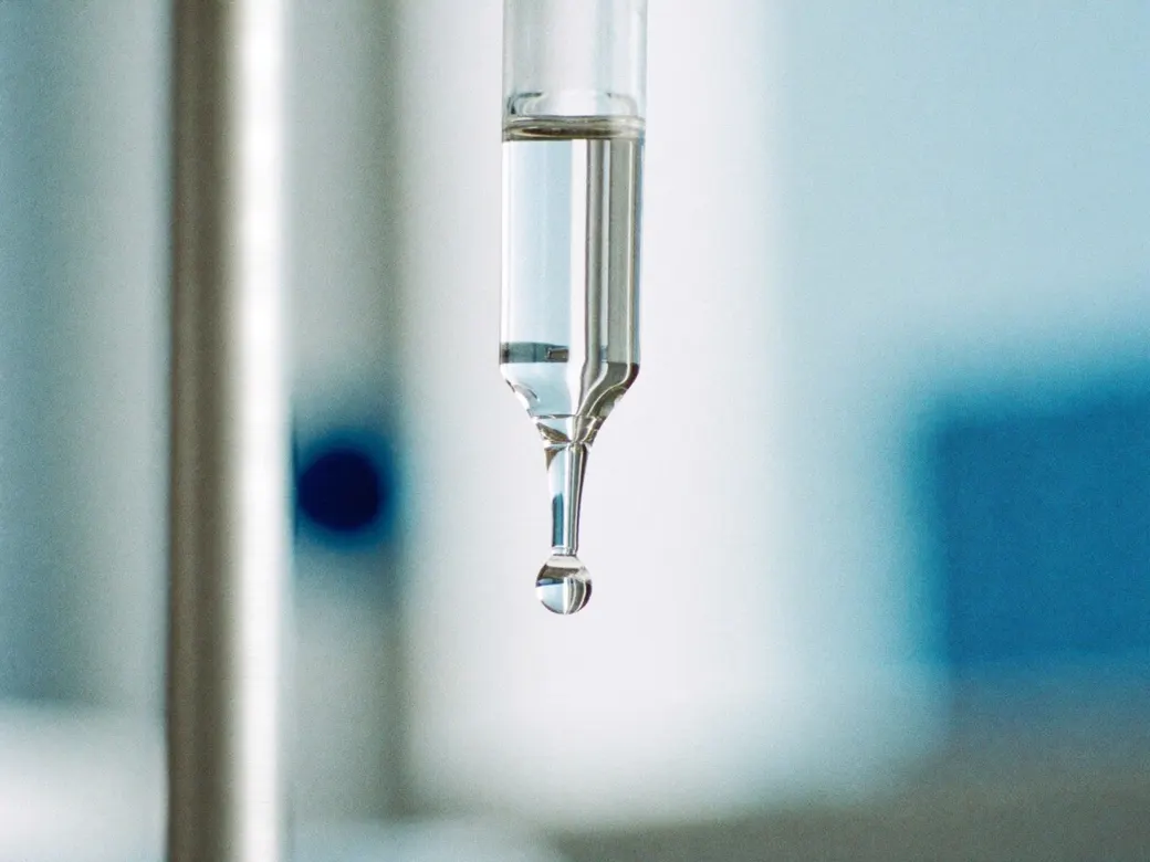 Una gota transparente a punto de caer de una pipeta de vidrio
